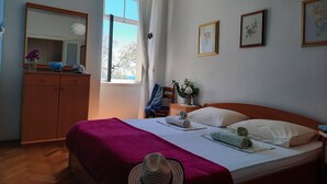 Un dormitorio con cama, cómoda, ventana con cortinas y cuadros en la pared.