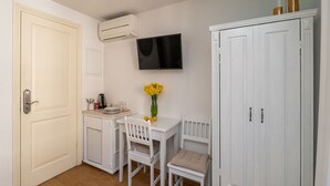 Een kleine, witte kamer met een kitchenette, een aan de muur bevestigde televisie en een kast met twee deuren.