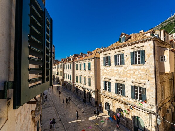 A historic street with stone buildings, a clear blue sky, and people walking.