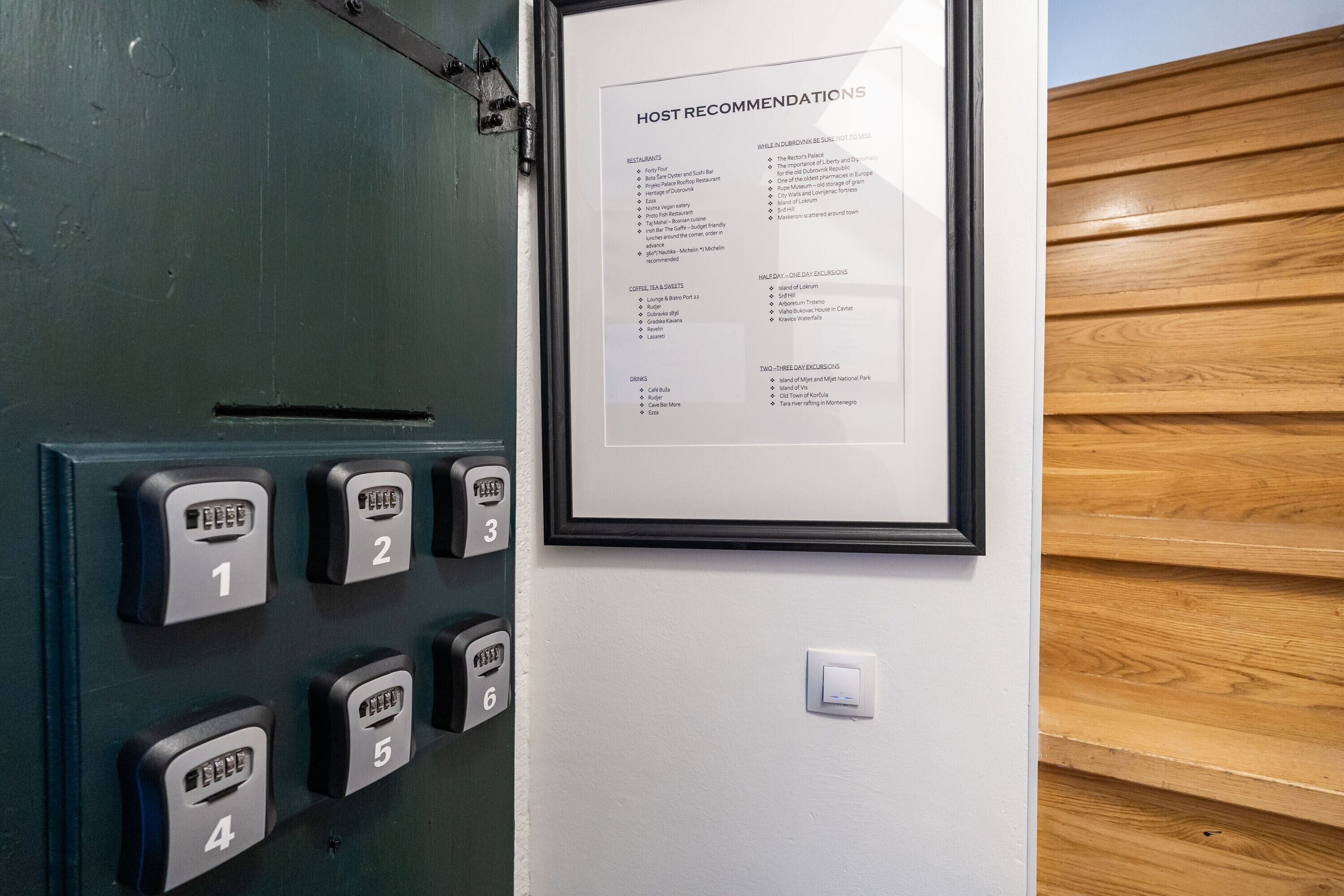 A hotel room with a door featuring a keycard entry system and a framed 'HOST RECOMMENDATIONS' sign listing local attractions and amenities.