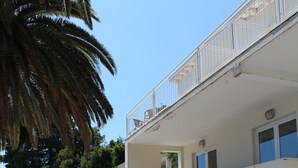 Un bâtiment à deux étages doté d’un balcon, d’un mur en béton agrémenté d’un parterre de fleurs et d’un palmier.