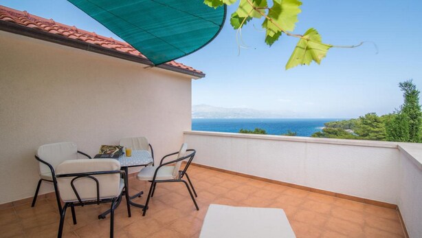 A balcony with a table and chairs, a view of the sea, and a green vine. - Apartments Ana & Bogdan - One Bedroom Apartment with Balcony and Sea View (A2) (ST) (Postira)