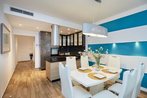 Une cuisine moderne avec un îlot central, une table à manger blanche agrémentée de sets de table dorés et un mur d’accent bleu.