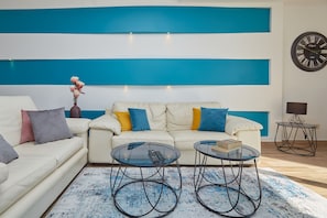 Un salon moderne avec un canapé blanc, deux petites tables rondes en verre et un mur d’accent aux couleurs bleu et blanc.
