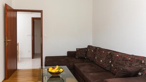 Ein Wohnzimmer mit einem braunen Sofa, einem Glastisch mit Obstschale und einer Holztür, die in einen anderen Raum führt.