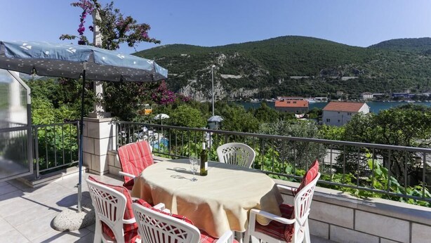 Ein Balkon mit Tisch und Stühlen, mit Blick auf eine Berglandschaft und ein Gewässer.