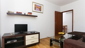 Ein Wohnzimmer mit Fernseher, einem Glastisch, einem braunen Sofa, Holzboden und einer Tür zu einem anderen Raum.