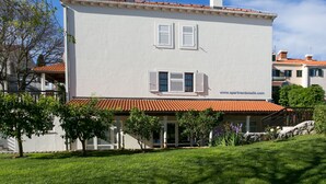 A two-story building with a white facade, red-tiled roof, and two windows with shutters.