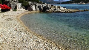 Ein Kiesstrand mit klarem Wasser, Felsformationen und einem entfernten Berg.