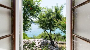 Blick durch ein Fenster auf eine Steinsäule und einen Baum im Vordergrund, mit Blick auf ein Gewässer.