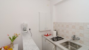 Une cuisine de taille réduite, avec des meubles blancs, une cuisinière à gaz, un évier et une machine à café.