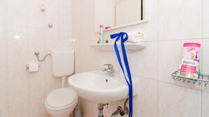 Une salle de bain équipée de toilettes, d’un lavabo et d’une étagère où sont rangés les articles de toilette.