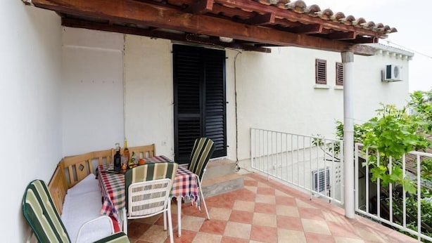 Un balcón con suelo a cuadros, una pérgola de madera, una mesa con sillas y un sofá.