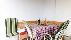 Un pequeño espacio al aire libre para comer con mantel a cuadros, dos sillas a rayas y un banco de madera.