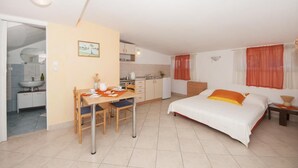 A compact hotel room with a bed, a small kitchen area, and a dining table. - Apartments Jasenka - Studio Attic with Terrace and Sea View (Supetar)