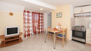 A compact living space with a kitchenette, a dining area with a table and chairs, a television, and a patterned curtain. - Apartments Jasenka - Studio Attic with Terrace and Sea View (Supetar)
