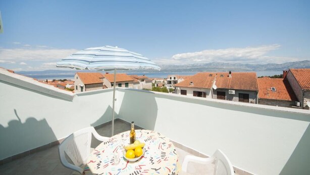 A balcony with a table, chairs, and a striped umbrella. - Apartments Jasenka - Studio Attic with Terrace and Sea View (Supetar)