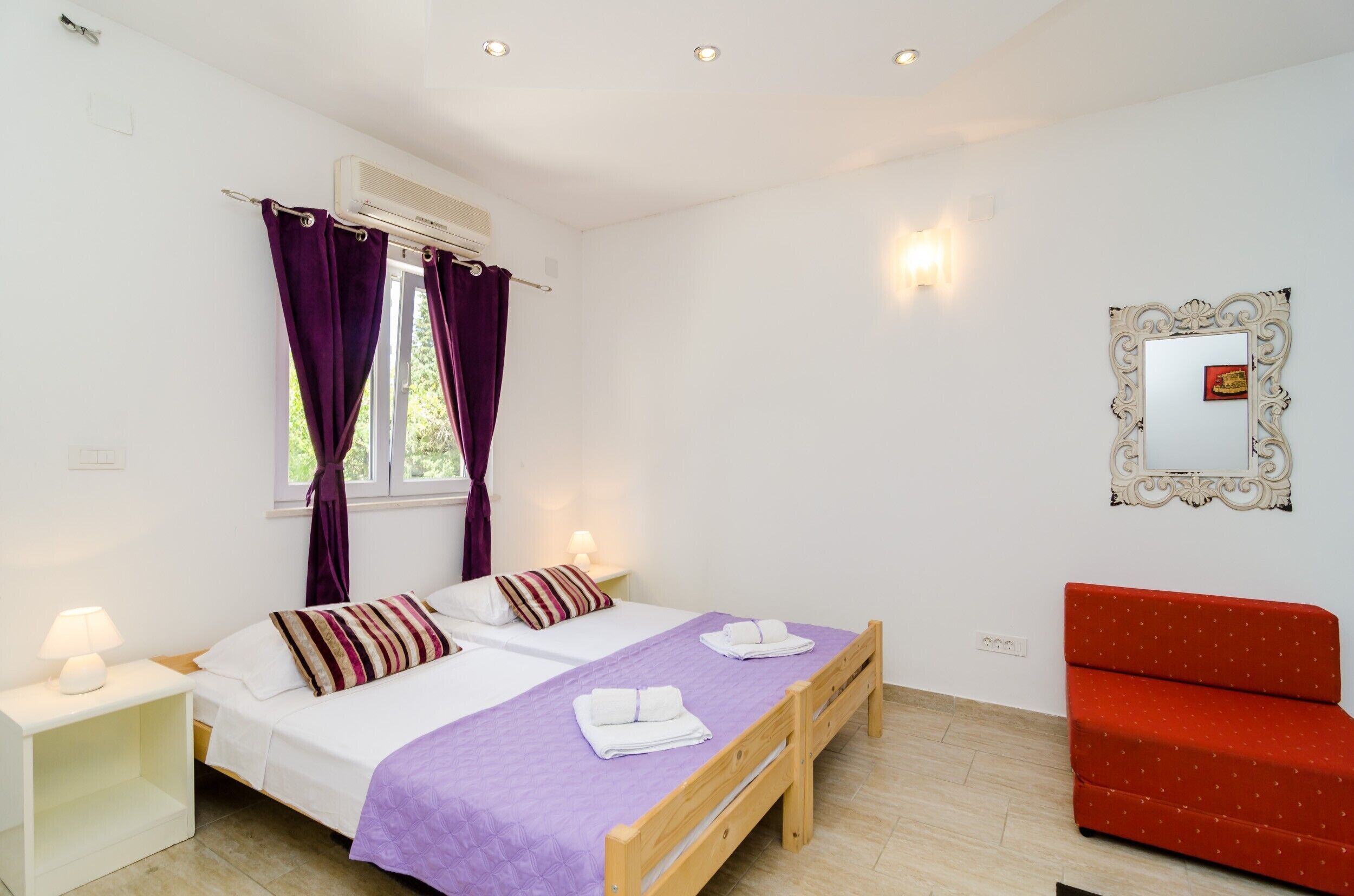 A bedroom with two beds, a red sofa, an air conditioner, and a mirror on the wall.