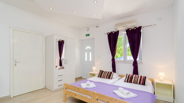 Ein Schlafzimmer mit einem hölzernen Bett, einem weißen Kleiderschrank und einem Fenster mit violetten Vorhängen.