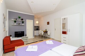 Quarto de hotel moderno com televisão, área de estar, mesa de jantar e guarda-roupa.