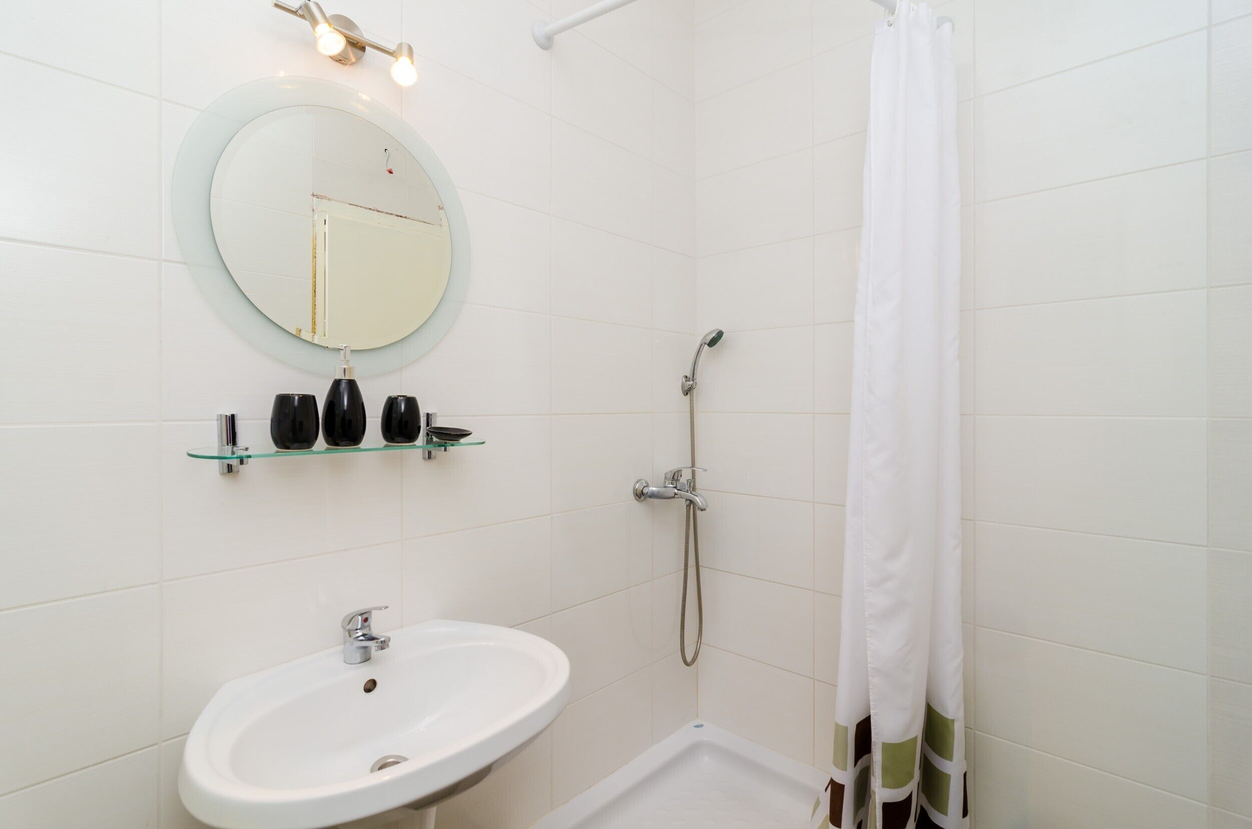 Een badkamer met een witte wastafel, een ronde spiegel en een douchecabine met een wit gordijn.
