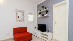 Ein Zimmer mit einem roten Sofa, einem Fernseher auf einem weißen Schrank, einem Spiegel und Regalen mit Dekoration.