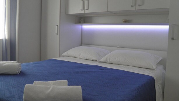 Quarto de hotel com uma cama, almofadas brancas, um edredom azul e toalhas brancas.