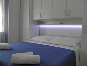 Una habitación de hotel con una cama, almohadas blancas, una colcha azul y toallas blancas.