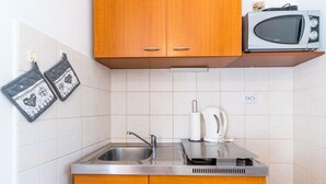 A small kitchen with wooden cabinets, a stainless steel sink, a microwave, and a kettle. - Studio Maro - Studio Apartment with Terrace (Dubrovnik)