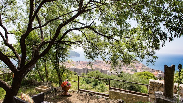 A terrace with wicker furniture, a stone wall, and a view of a coastal town. - Studio Maro - Studio Apartment with Terrace (Dubrovnik)