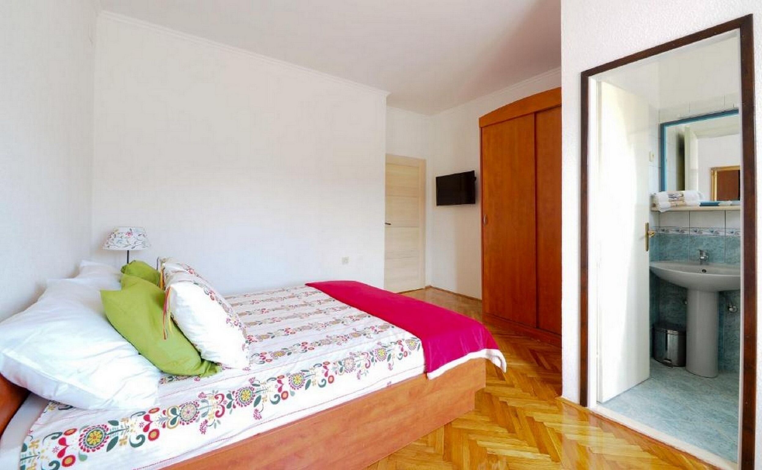 Ein Schlafzimmer mit Bett, Nachttisch, Spiegel und angrenzendem Badezimmer, das durch eine offene Tür sichtbar ist.