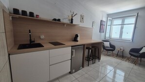 Een moderne keuken met een vaatwasser, een spoelbak en een koffieapparaat. Twee barkrukken en een kleine tafel met een fotolijstje.