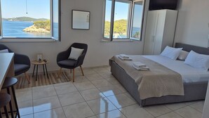 Een slaapkamer met een bed, een stoel, een bureau en uitzicht op zee.