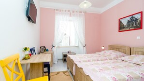 Ein Schlafzimmer mit einem Bett, einem Schreibtisch, einem Stuhl, einem Fernseher und einem Fenster mit Vorhängen.