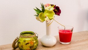 Ein grünes Glasgefäß mit Seilkordel, eine weiße Vase mit Blumen und eine rote Kerze auf einer Holzoberfläche.