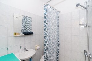 Un baño con ducha, lavamanos, espejo y toallero.