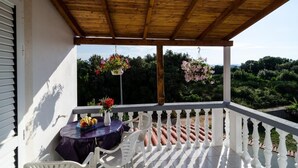 Ein überdachter Balkon mit Tisch und Stühlen, Blick ins Grüne und hängende Blumenkörbe.