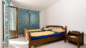 Ein Schlafzimmer mit einem hölzernen Bett, einem Nachttisch und einem Fenster mit floralem Vorhang.