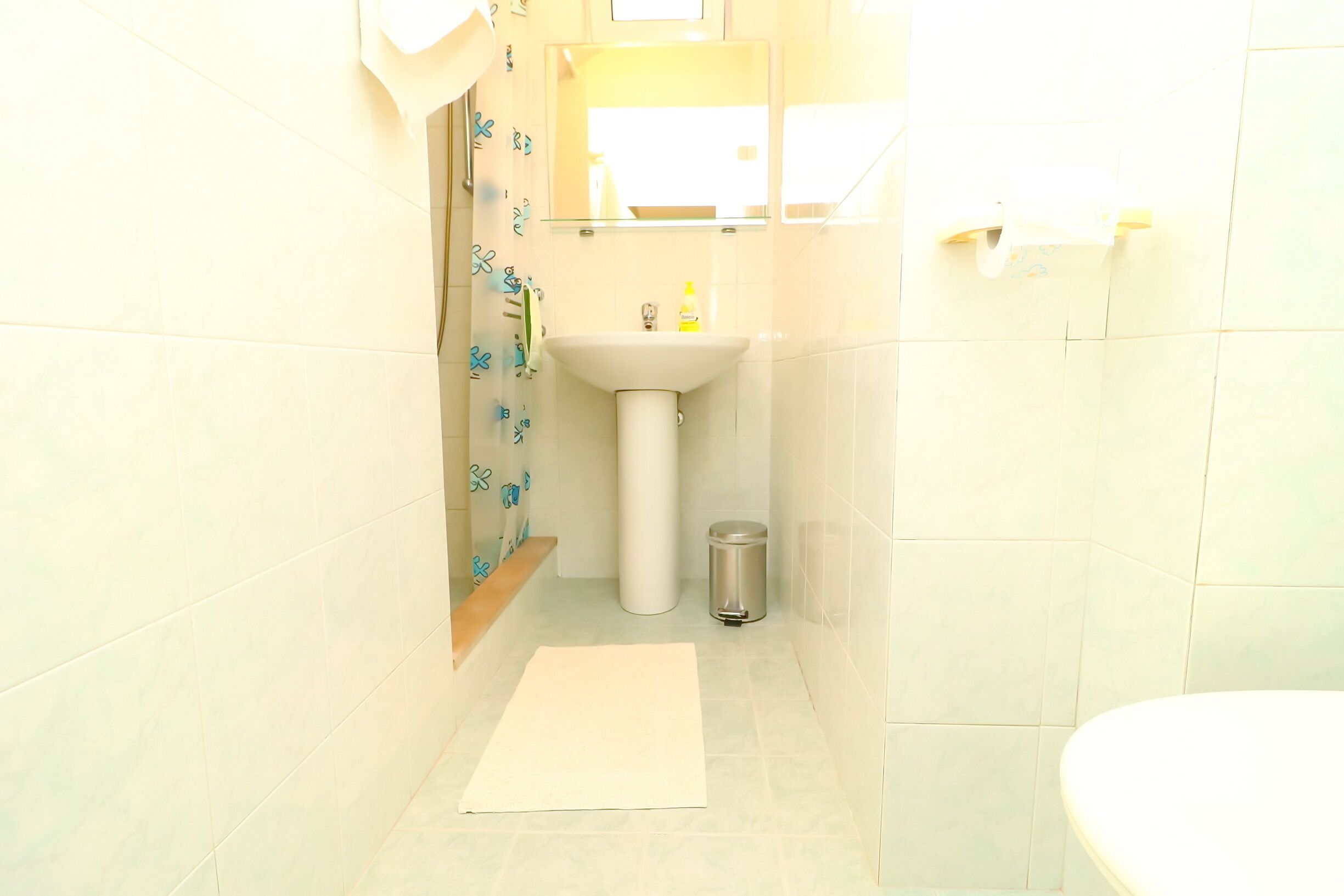 Ein Badezimmer mit einem weißen Waschbecken, einem Spiegel darüber und einer Mülltonne rechts.