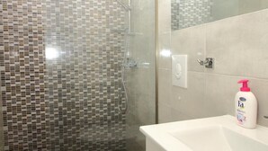 A bathroom with a glass-enclosed shower, a white toilet, and a sink with a mirror.