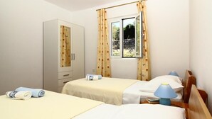 A room with two beds, a wardrobe, a window with curtains, and a lamp.