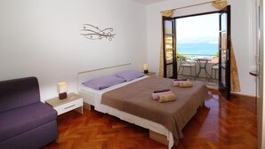 A bedroom with a bed, a nightstand, a purple sofa, and a view of the sea through an open door.