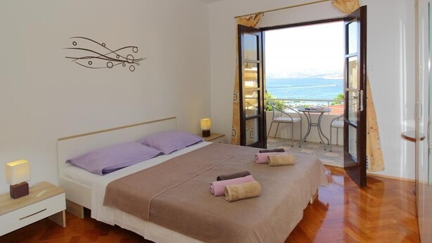 A bedroom with a bed, bedside tables, a decorative wall piece, and a view of the sea through an open door.