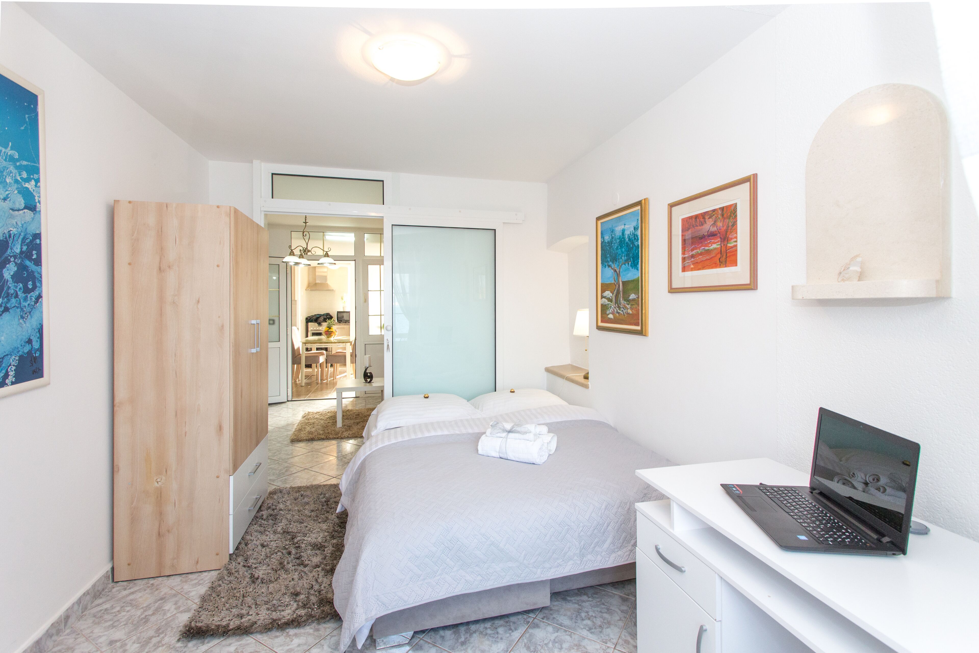 Une chambre d’hôtel moderne, équipée d’un lit, d’un bureau avec un ordinateur portable et d’œuvres d’art accrochées aux murs.