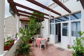 Une terrasse avec une table et des chaises, entourée de plantes en pot et agrémentée d’une pergola.
