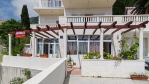 A building with a white exterior, a wooden pergola, and a sign indicating 'Apartments Mama Mia'.
