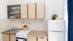 A compact kitchen with a built-in oven, a refrigerator, and a glass-fronted cabinet with kitchenware.