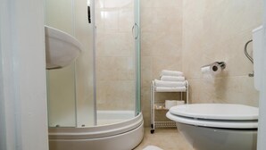 Une salle de bain avec une douche à parois de verre, des toilettes et une étagère avec des serviettes.