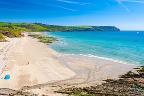 A beach with clear blue water, a sandy shore, and distant hills. - Trewhiddle Cottage 42 (St Austell)