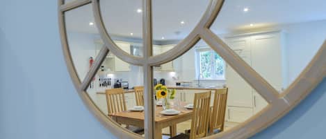 A dining area with a round mirror reflecting a kitchen and dining table set with plates, cutlery, and a vase of sunflowers.